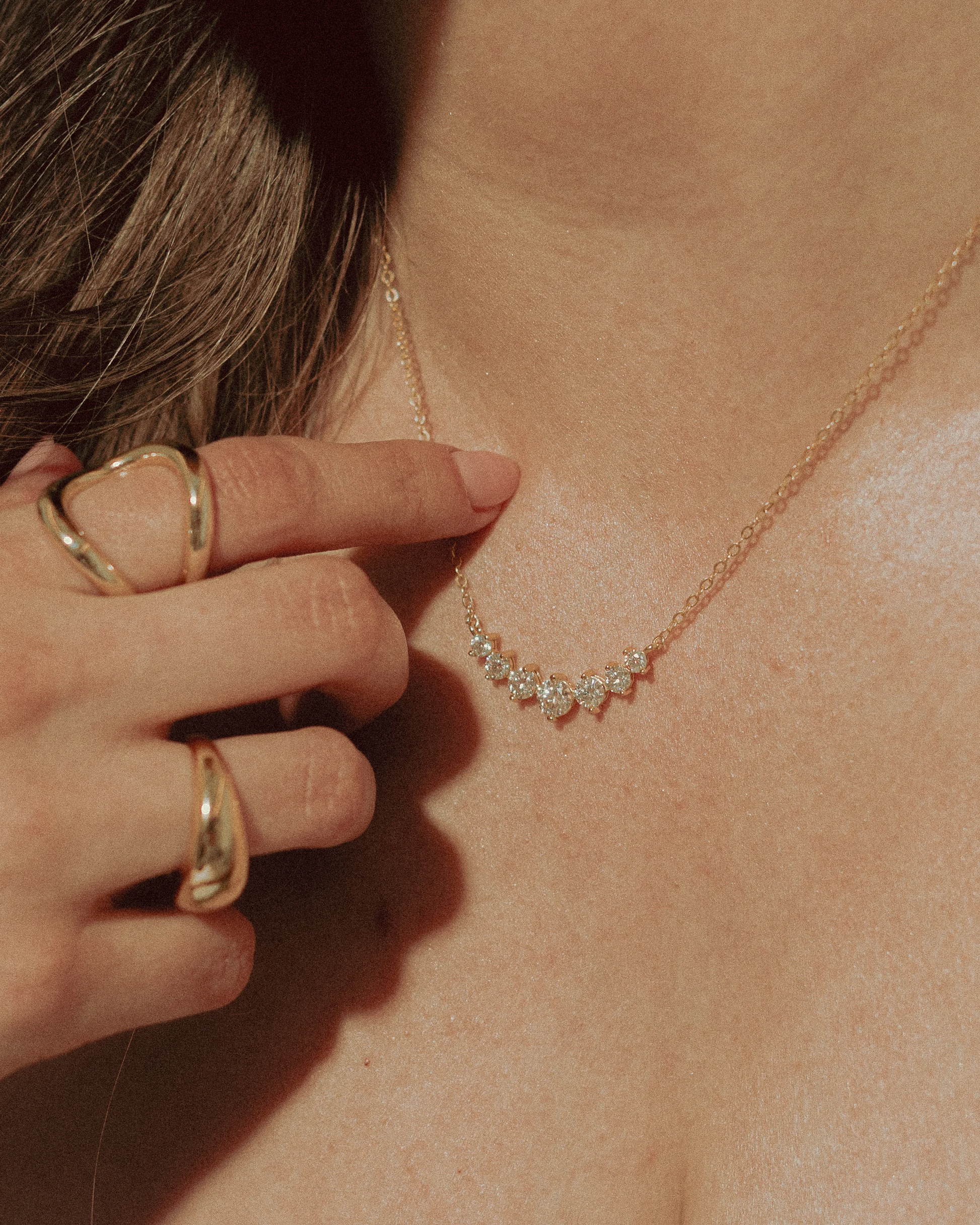 Close-up of Goldmacher moissanite charm  Felis necklace paired with gold bold dome and swirl rings on model's hand