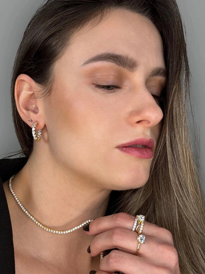 Hands-focused photo showing Goldmacher moissanite heart, pavé, and V-shaped rings, with hoop earrings and tennis chain
